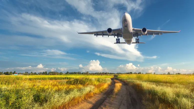 Passenger plane flying low over grassy field.