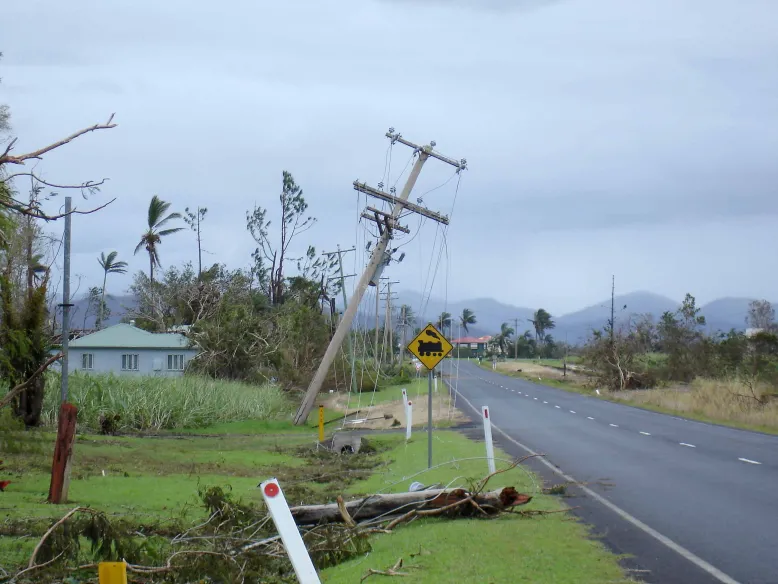 Telephone pole blown over and debris beside road following a cyclone.