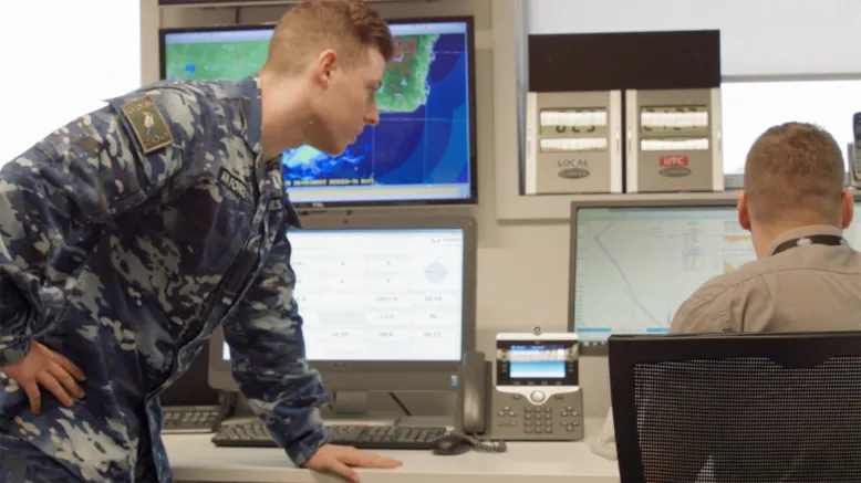 Air Force officer works with Bureau staff member in front of computer screens.