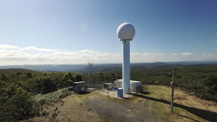 White weather radar on top of a bare hill, surrounded by forest.