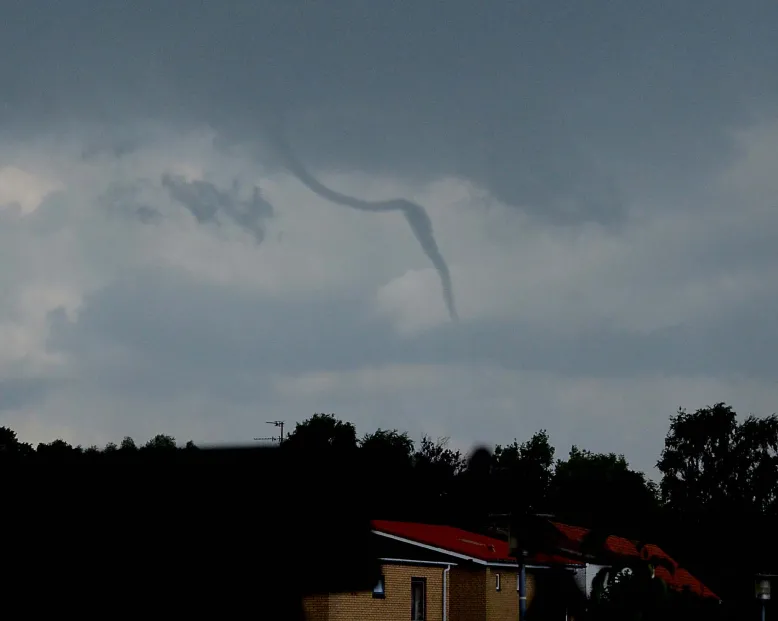 Tornado spinning in a grey sky above a suburban street.