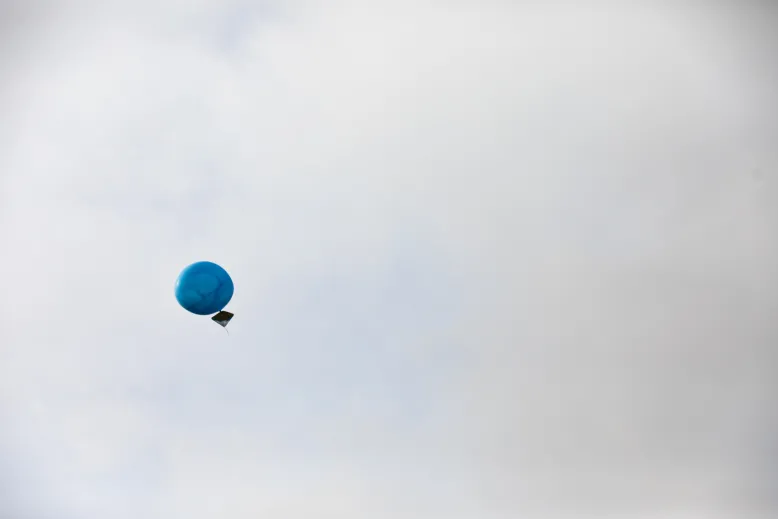 Weather balloon in flight against an overcast sky with cardboard target attached.