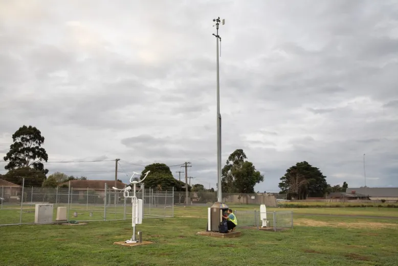 Technician squats at the bottom of a tall weather station to carry out maintenance.