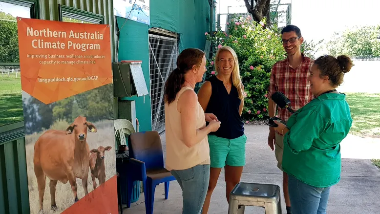 Twp women and a man are interviewed by a female reporter holding a microphone, outside a building and in front of a banner that says 'Northern Australia Climate Program'.