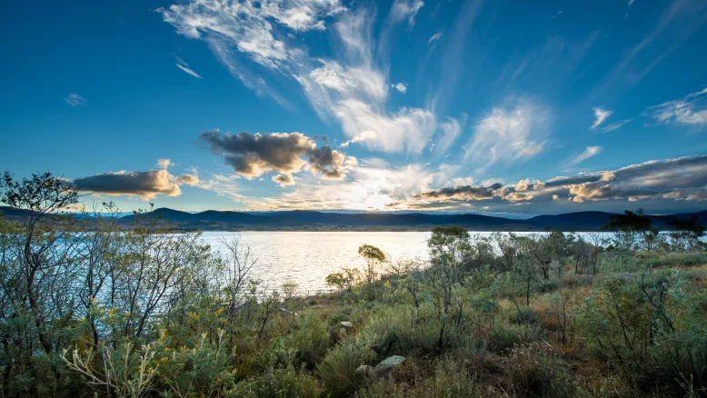 Dramatic late afternoon photo of Lake Jindabyne with low bushland in foreground.