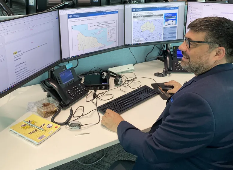 Meteorologist at workstation surrounded by computer screens.