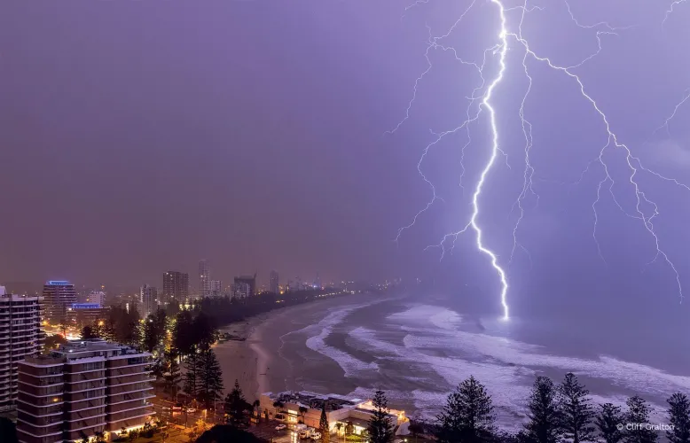 Bright, glowing thunderbolt lights up a beachfront cityscape as it strikes the ocean.