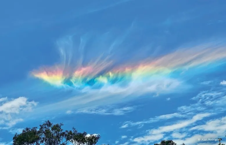 Thin, wispy clouds are dyed in the colours of a passing rainbow.