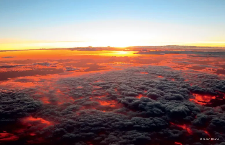 Setting sun turns a sea of thick clouds red and orange from underneath, as if they were a blanket of heat and smoke.