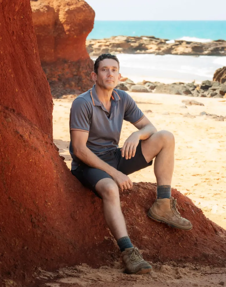 Photographer Kane McLatchie sits on a rock with the ocean in the background.