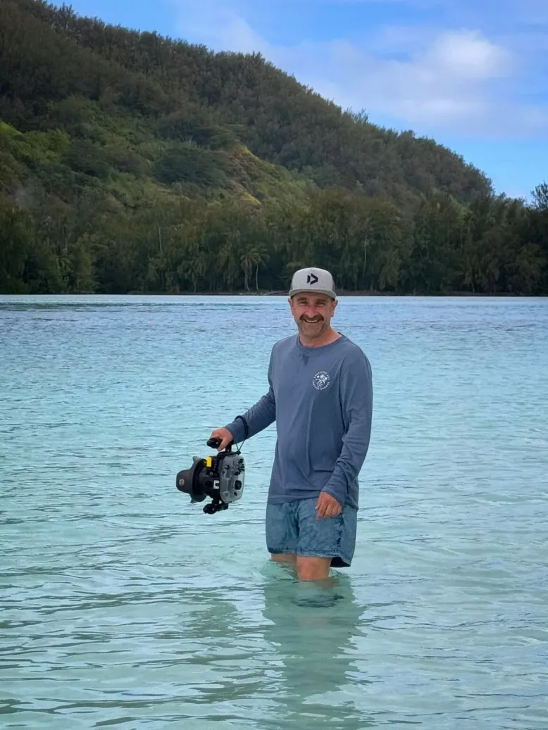 Photographer Rob Embury stands in the ocean while holding a large camera