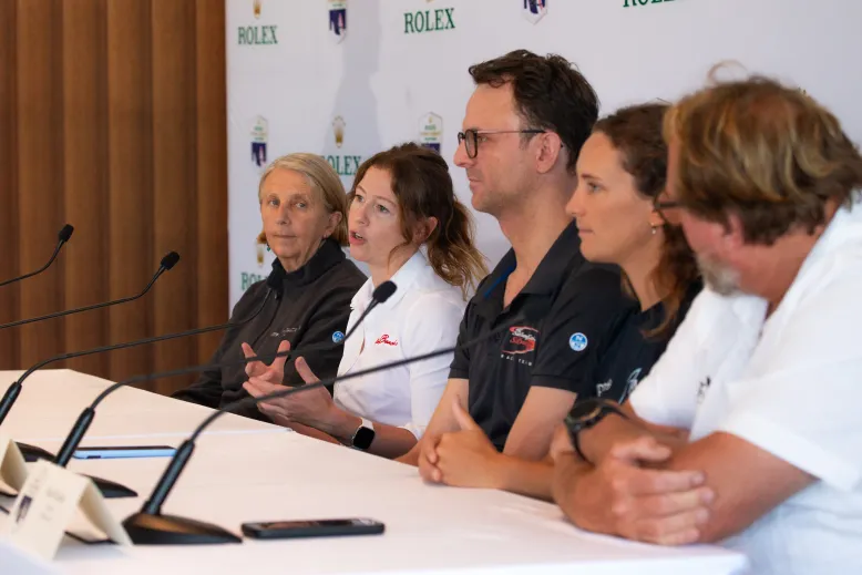 Panel of people seated at a table with microphones during a media conference, with a backdrop featuring Rolex branding.