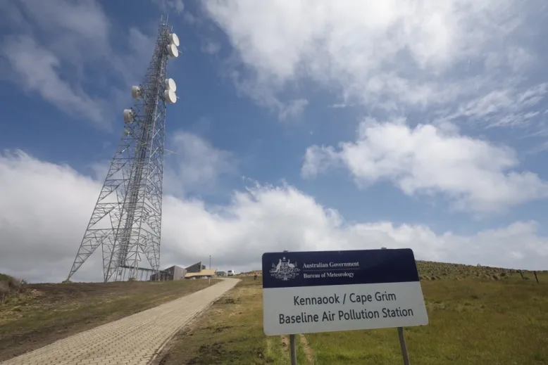 Green hill with a sign and radio tower on it, with a blue sky and clouds