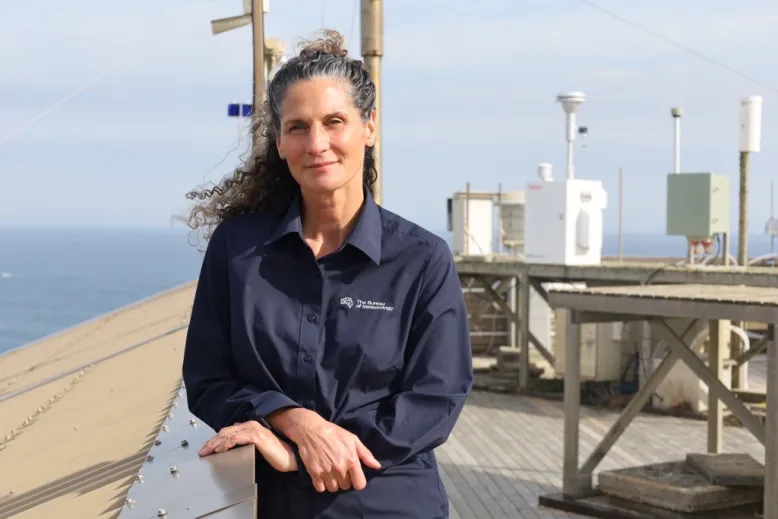 Bureau of Meteorology station manager stands in front of measuring equipment outside