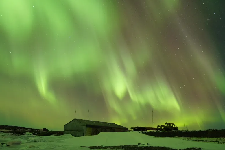 Aurora australis appearing as ribbons of green light above a station in Antarctica.