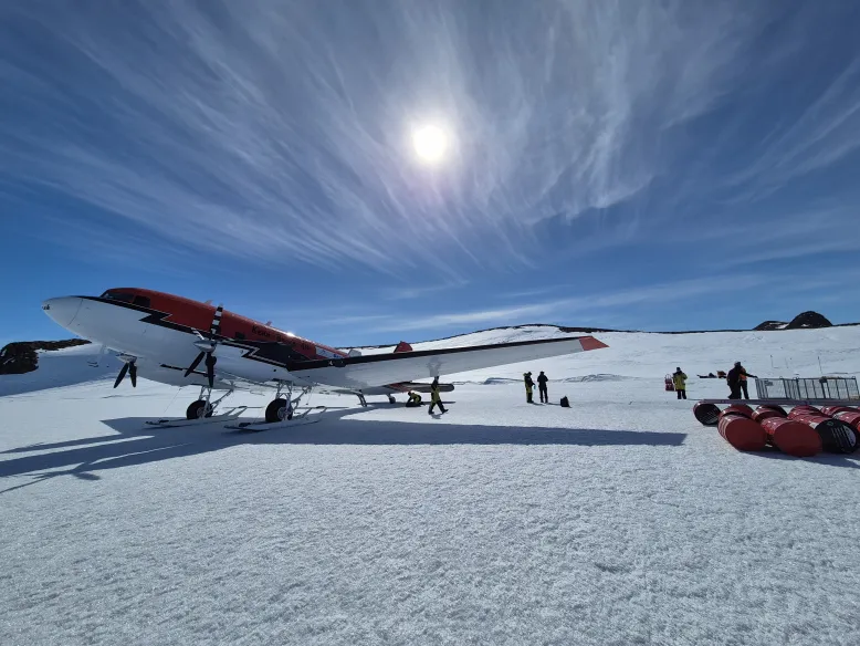 Small aircraft parked on ice in Antarctica with several people in winter gear.