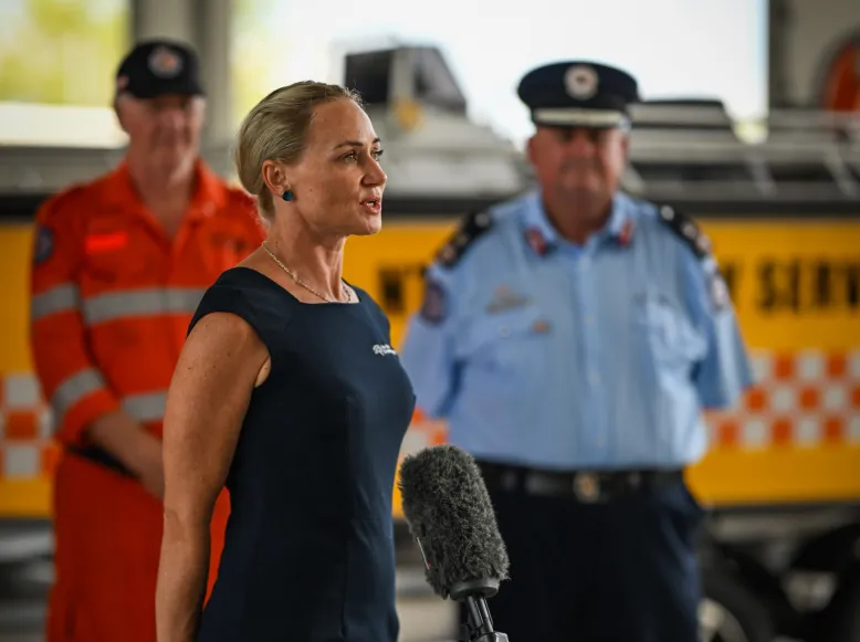 NT Manager speaking into microphone with two emergency servicemen in the background.