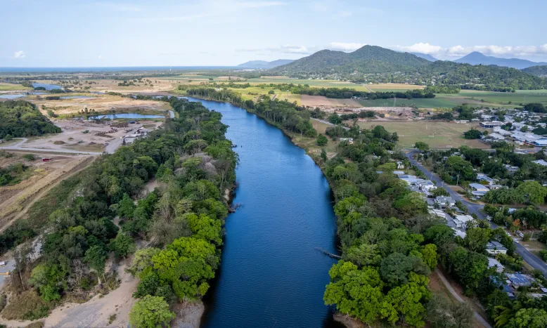 Aerial drone view of Barron River in Cairns, Queensland, bordered by dense vegetation, and forested mountains in the background.