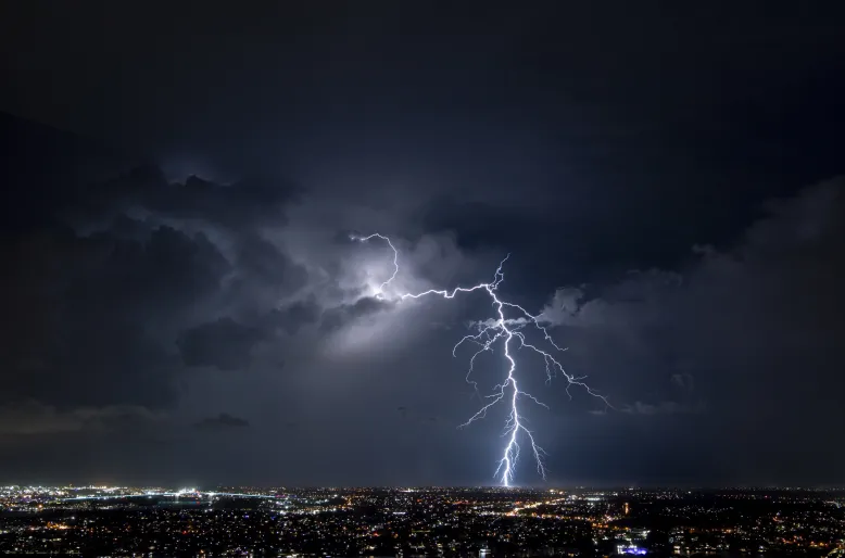 Lightning strike behind dark storm clouds above a city skyline.