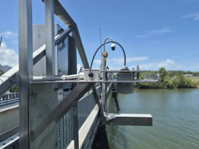 Water level radar mounted on a metal monitoring structure above a river, with water and vegetation visible in the background.