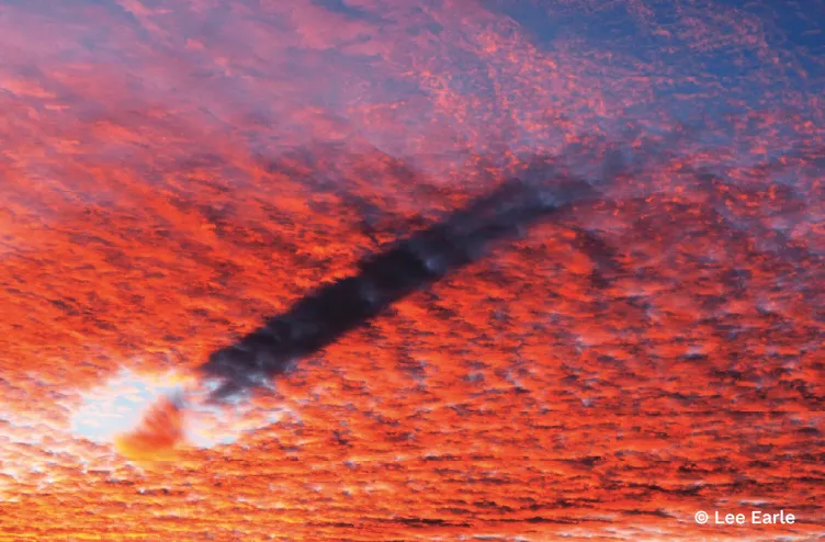 Vivid red and orange cloud layers glow at sunset as a dark cloud band sweeps diagonally across the sky.