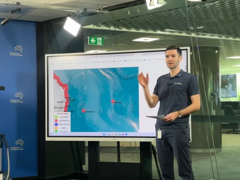 Male meteorologist presents in front of a large touch screen for a mock simulated tsunami exercise.