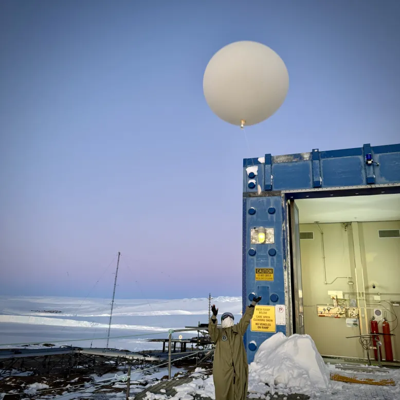 Person releasing a weather balloon beside a building in a snowy Antarctic environment.