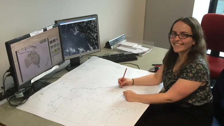 Person working at a desk with weather maps and satellite imagery displayed on computer monitors.