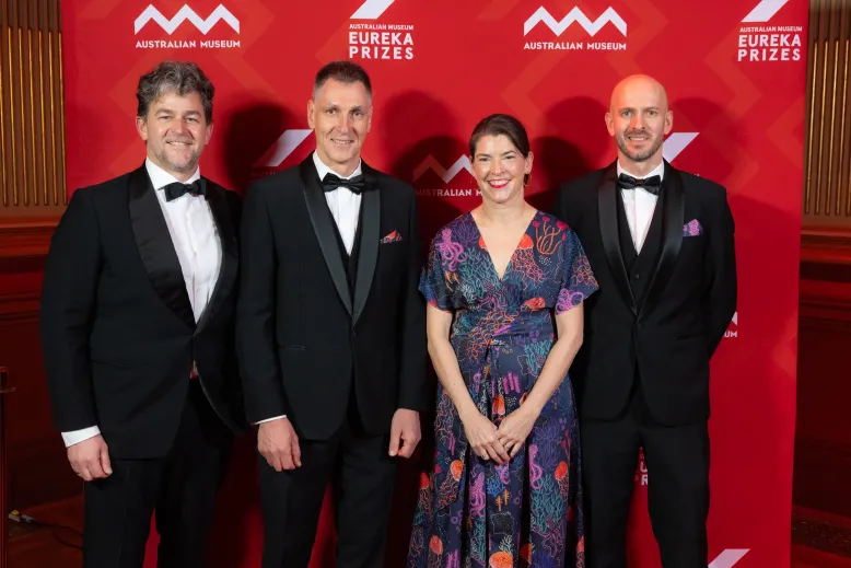 Four people in formal eveningwear stand in front of an Australian Museum Eureka Prizes media wall.