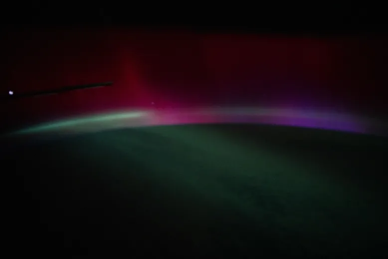 Aurora-like bands of red, purple and green light arc above Earth's curved horizon as seen from space.